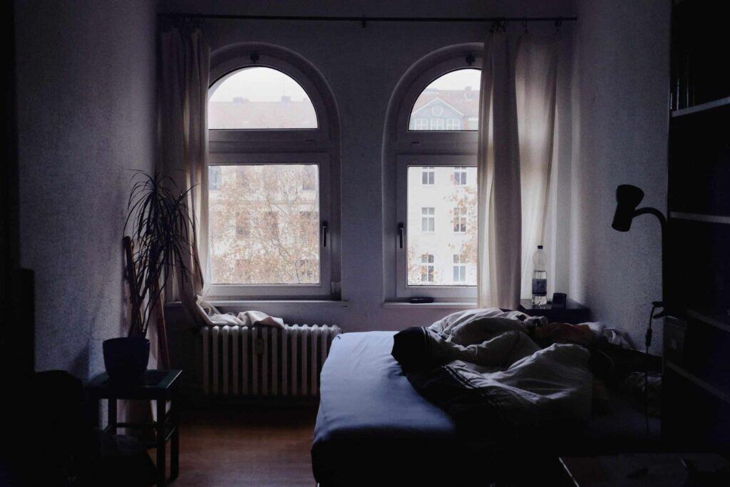 A cozy bedroom with a gently rumpled bed, a cheerful potted plant, and sunlight filtering through two arched windows that frame views of trees and nearby buildings. Trust Bell Brothers—serving Northern California communities with background-checked technicians, upfront pricing, and our No Surprise Guarantee for comfort you can count on.