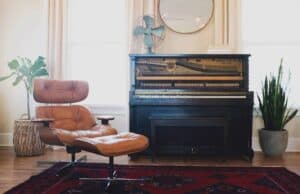 A bright, modern living room showcases a brown leather lounge chair and ottoman beside a black upright piano with exposed strings, accented by lush potted plants. Choose Bell Brothers for trusted service in Northern California—our background-checked technicians provide upfront pricing with our No Surprise Guarantee, earning us a strong reputation across local communities.
