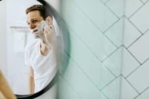 A man confidently shaves his face while looking into a round bathroom mirror, illustrating the comfort and peace of mind you can expect with Bell Brothers. Our trusted, background-checked technicians provide expert service with upfront pricing and our No Surprise Guarantee—earning us a strong reputation in Northern California communities.
