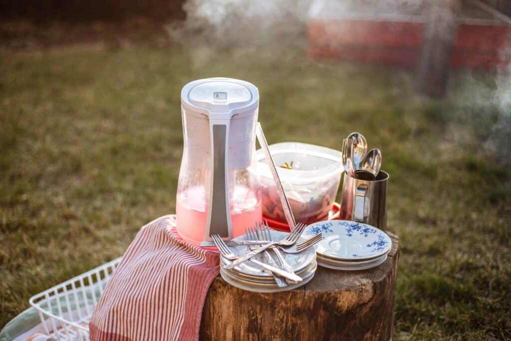 Outdoor tableware arrangement featuring a water pitcher, plates, forks, a striped towel, and a bowl set atop a tree stump. A drying rack and gentle steam or smoke appear in the background. Trust Bell Brothers—serving Northern California with our No Surprise Guarantee, background-checked technicians, and upfront pricing. Count on our strong reputation for reliable service in your community.