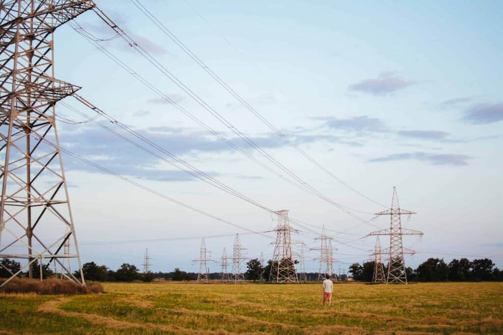 A friendly, background-checked Bell Brothers technician stands in a grassy field beneath high-voltage power lines and transmission towers on a partly cloudy day. With our No Surprise Guarantee, upfront pricing, and trusted reputation across Northern California communities, you can rely on us for professional and dependable service every time.