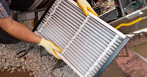 Image: a man changing out an HVAC filter.