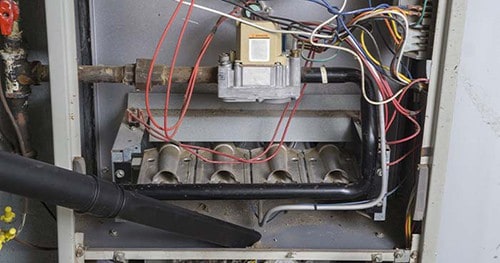 Image: someone vacuuming out the inside of a furnace.