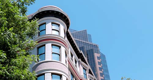 Image: a historic Victorian home with a modern office building in the background.