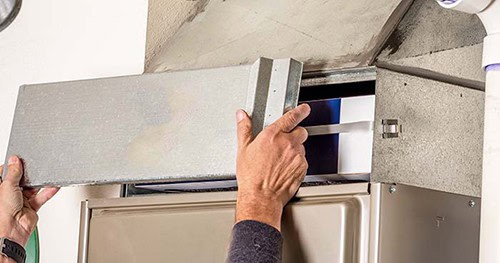 Image: an HVAC tech putting the cover back on the filter slot.