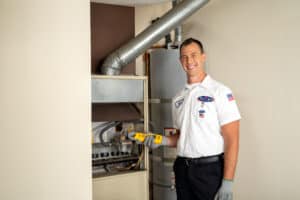 A Bell Brothers technician, dressed in uniform and ready with professional tools, stands beside an open furnace and water heater in a home's utility room—prepared to provide thorough furnace maintenance and ensure your home is cozy for winter. With our trusted No Surprise Guarantee, background-checked technicians, upfront pricing, and outstanding reputation throughout Northern California communities, you can count on Bell Brothers for service you can trust.