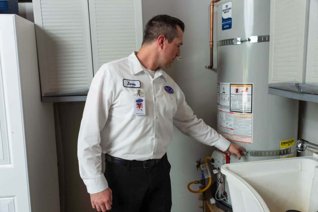 A Bell Brothers pro in a white uniform inspects a water heater, ensuring comfort with upfront pricing and our No Surprise Guarantee.