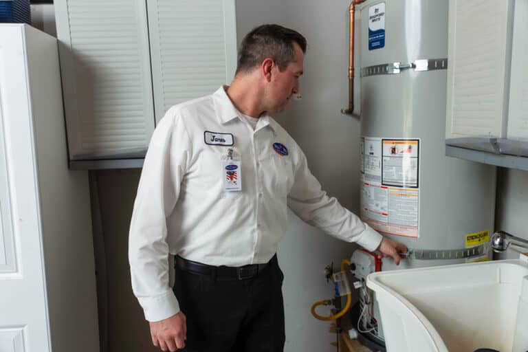 A Bell Brothers pro in a white uniform inspects a water heater, ensuring comfort with upfront pricing and our No Surprise Guarantee.
