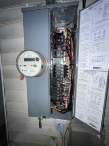 An open electrical panel in Sacramento shows circuit breakers and wiring, with Bell Brothers' No Surprise Guarantee spec sheet attached.