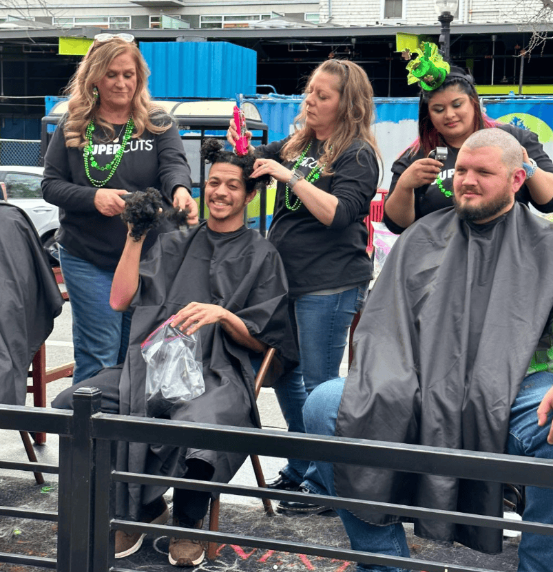 Smiling clients enjoy outdoor haircuts at a festive Bell Brothers event, showcasing trusted service and transparent, upfront pricing.