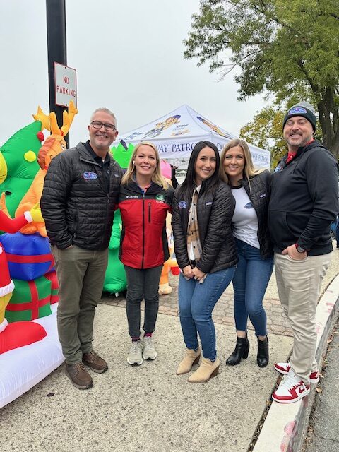 Five Bell Brothers pros smile by a holiday inflatable, reflecting trusted service, upfront pricing, and our No Surprise Guarantee.