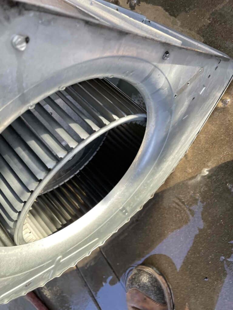 A metal industrial fan from a Furnace Tune-Up sits on a wet floor, with a technician’s boot—Bell Brothers’ trusted, upfront service.