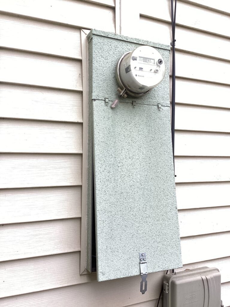 An electric meter on a home's exterior with its panel open, safely secured—ready for expert panel replacement by Bell Brothers.