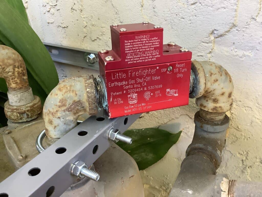 A Bell Brothers technician installs a red "Little Firefighter" gas shut-off valve on a braced metal pipe—upfront pricing, No Surprise Guarantee.