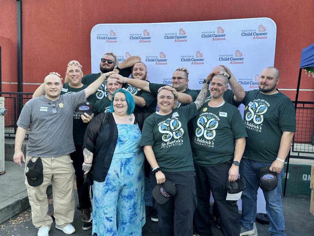 Friendly, trusted team members with shaved heads smile by the Keaton’s Child Cancer Alliance logo, reflecting our No Surprise Guarantee.