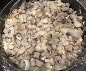 Pokrojone śledzie dodane do warstwowej sałatki leśnej polanej ze śledziem