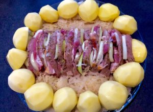 ziemniaki ułożone wokół schabu faszerowanego kapustą kiszoną