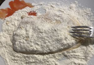 Panierowanie kebabowych sznycli drobiowych w mące przed smażeniem na patelni.