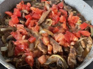 dodawanie bulionu i pomidorów do strogonowa z winem