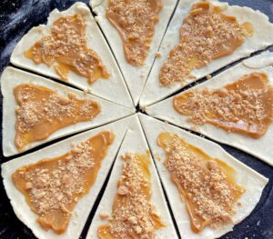 Posypywanie trójkątów ciasta solonymi orzeszkami do rogalików z kajmakiem