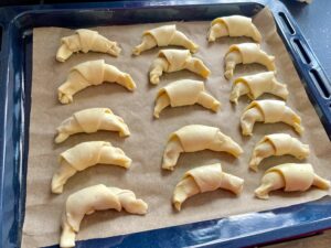 Surowe rogaliki z kajmakiem ułożone na blaszce wyłożonej papierem do pieczenia