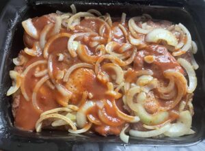 dodawanie cebuli i sosu do karkówki w ketchupie