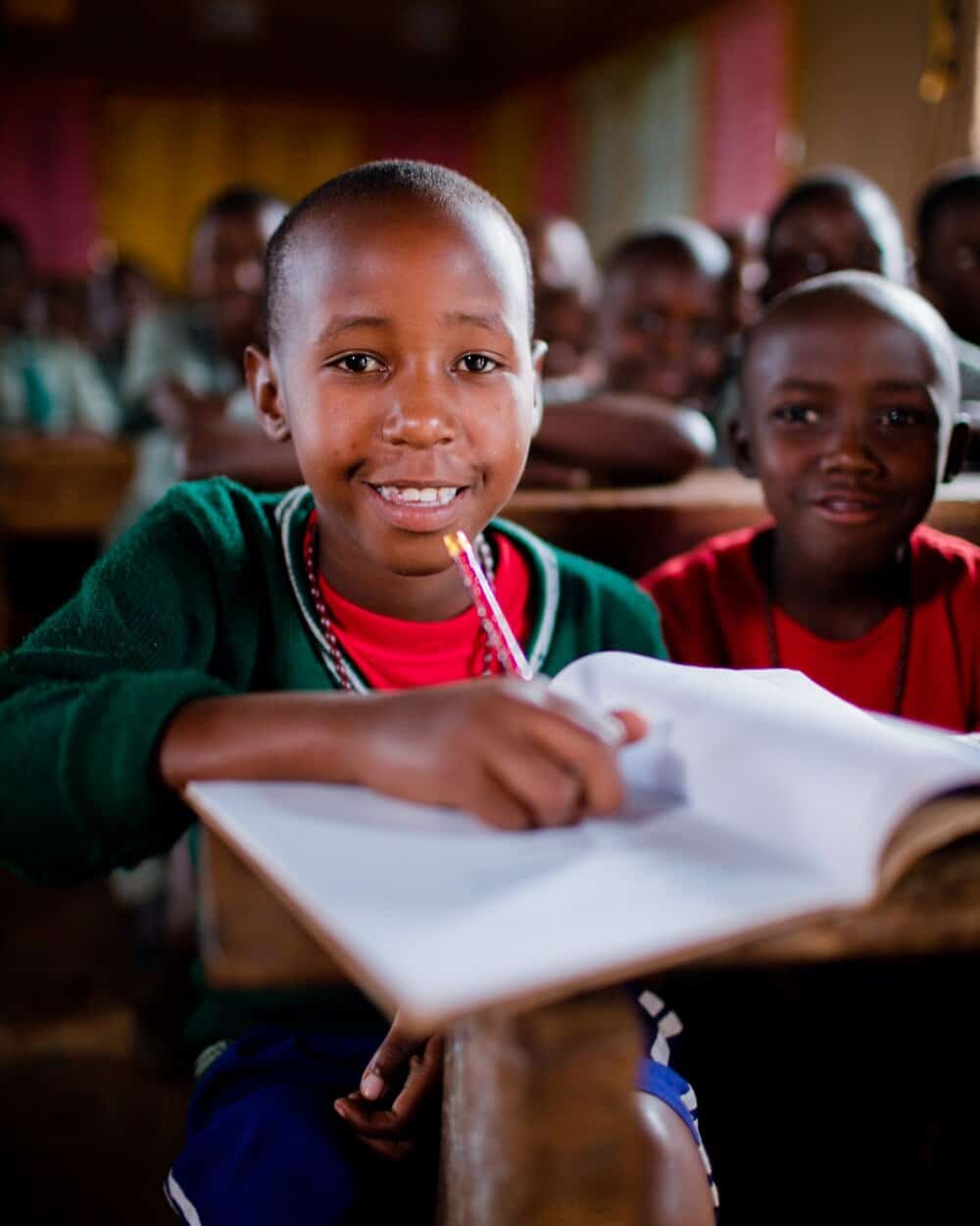 Student sitting in a classroom, writing in a notebook and smiling