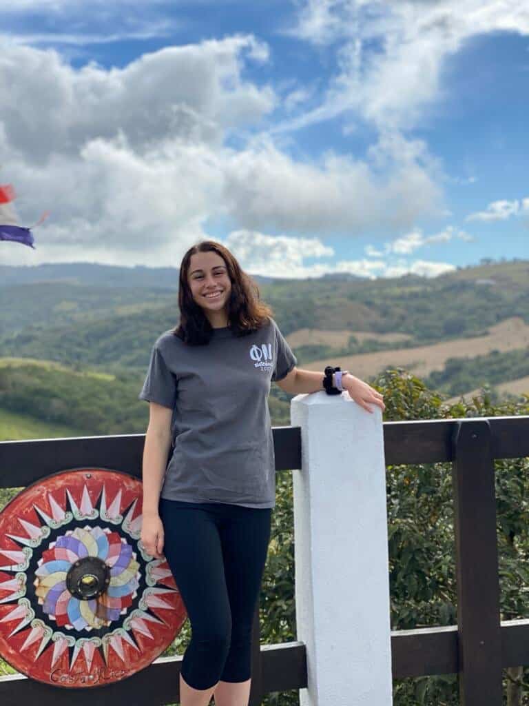 elena walker stands smiling in front of a fence with a mountain view in the background