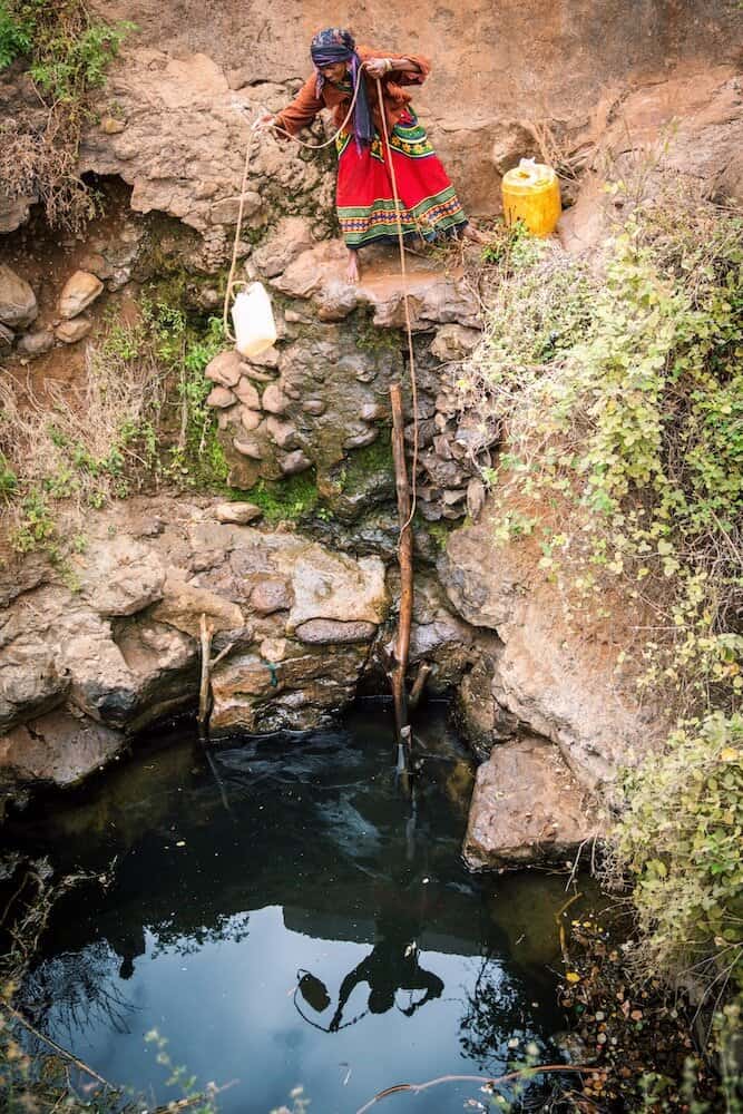 An African woman filling a water jug at a natural spring