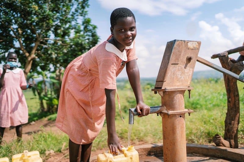 girl filling jerry can with water from well