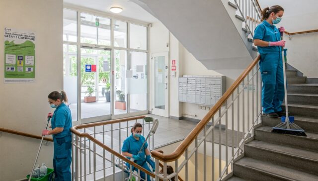 Reinigungsteam bei der Unterhaltsreinigung eines Berliner Treppenhauses, säubert Stufen, Geländer und Eingangsbereich.