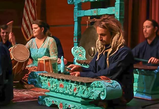 Max Berry playing with Gamelan Kembang Sunda with musicians sitting at their instruments on the stage floor.