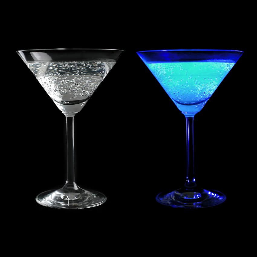 Two cocktail glasses of a bubbly liquid, one is clear, one is glowing blue
