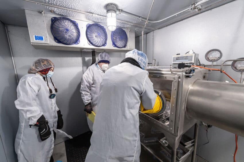 Three scientists in white lab coats and hair nets processing the apollo 17 samples in a glove box in a cold room
