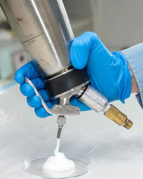 A gloved hand releases foam out of a siphon