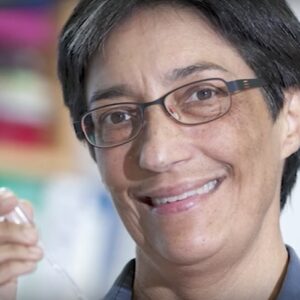 A woman with short black hair and glasses smiles at the camera