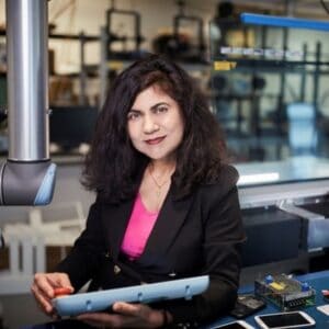 A woman with dark brown hair, wearing a pink top and black blazer.