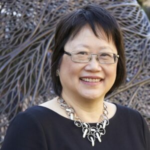 An older woman with short black hair, wearing glasses, smiles at the camera