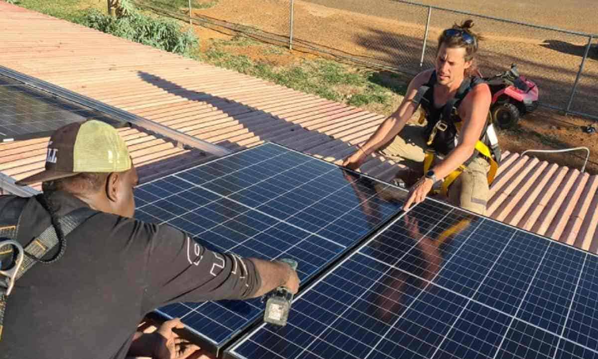 Two men position solar panels onto the roof of a house.