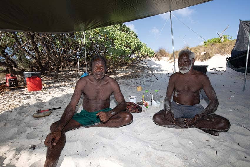Traditional owners david ganambarr and james djamu sit on the sand.