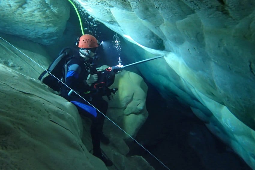 An underwater image of a man in diving gear, drilling into the wall of an underwater cave
