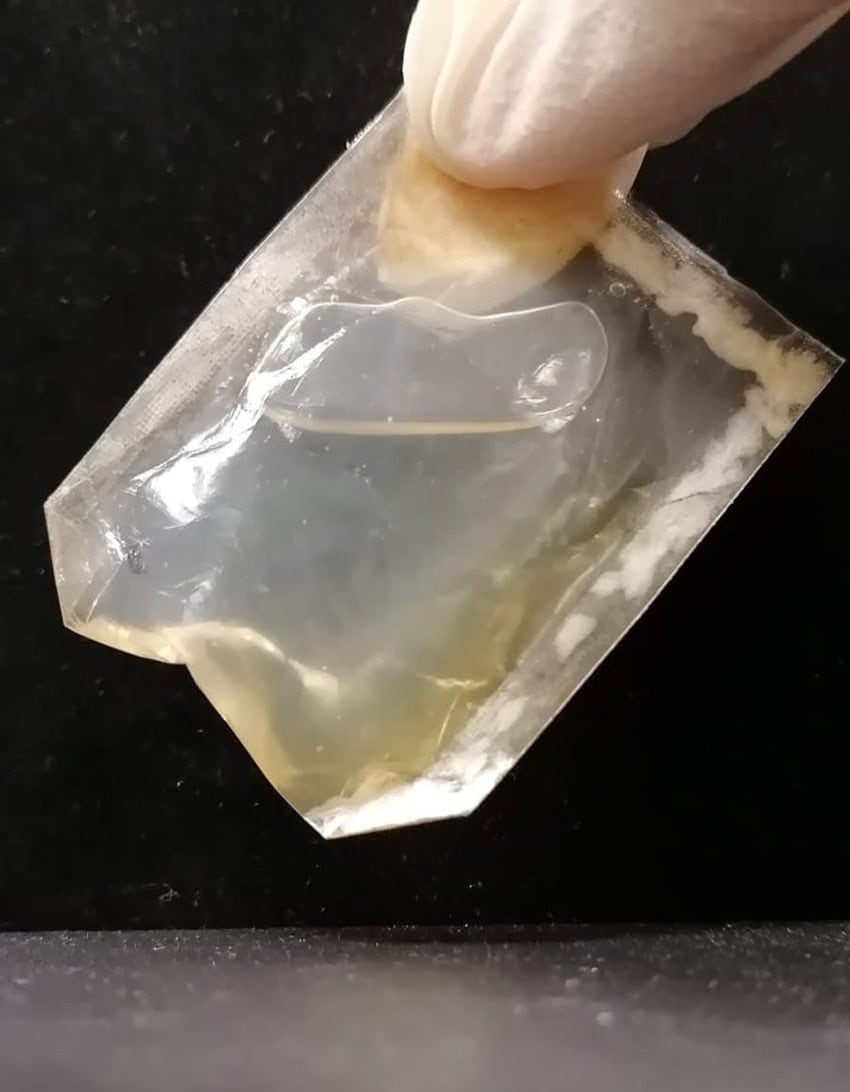 Gloved fingers hold a small, transparent package filled with oil