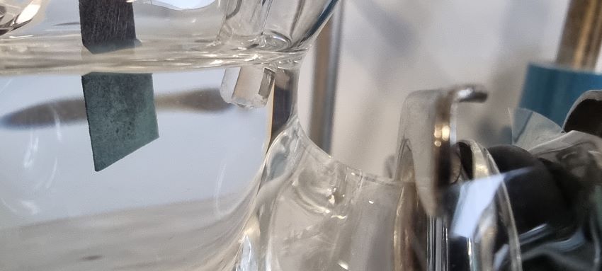 Close up of beaker filled with colourless liquid in lab, with small piece of metal added