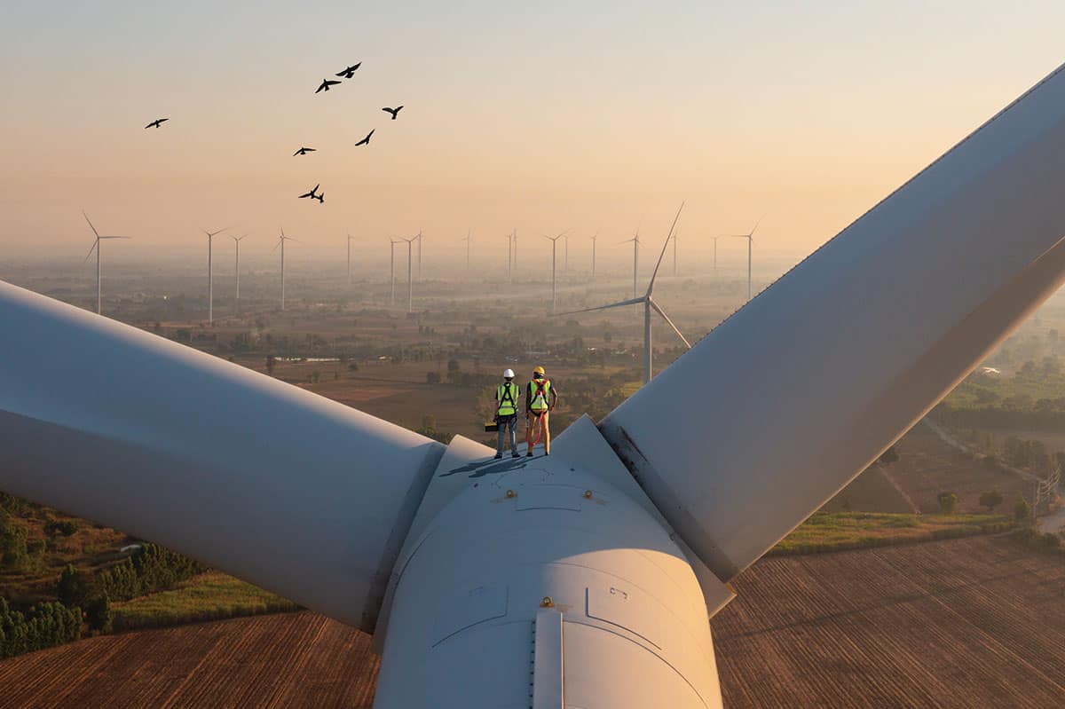Two people stand on top of a wind turbine.