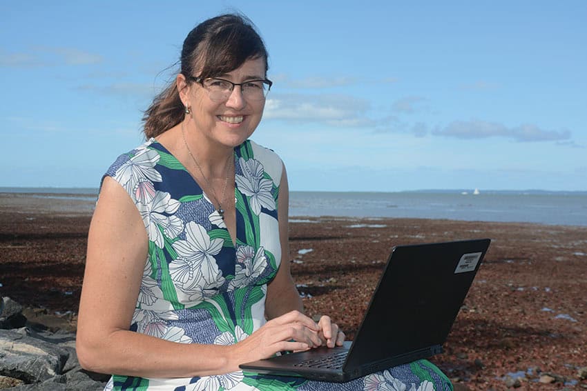 Eva plaganyi sits outside with her laptop.