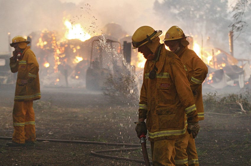 Three firefighters in full kit battle a bushfire.