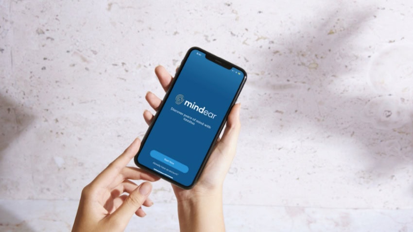 A photograph of a pair of hands holding a smartphone with the mindear app displayed on its screen