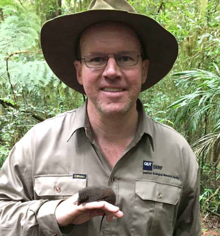 Person stands outside with tiny mammal on his arm smiling at camera