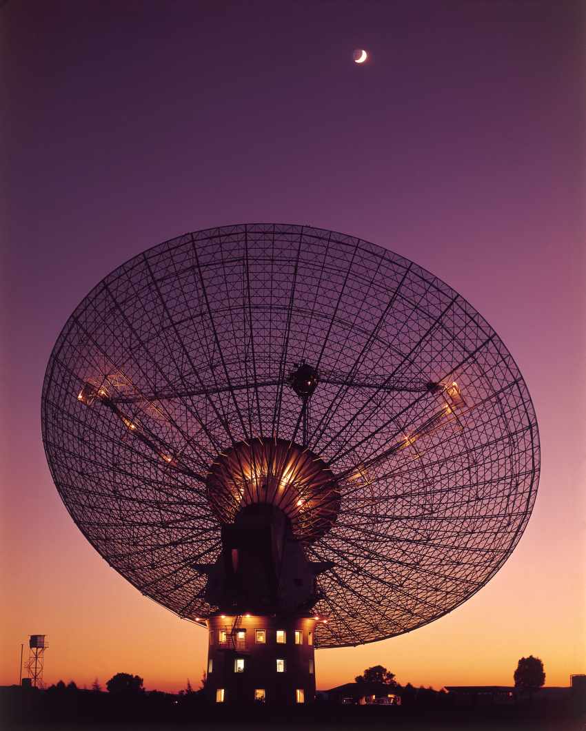A photo of a large telescope during a sunset, with the moon high in the sky