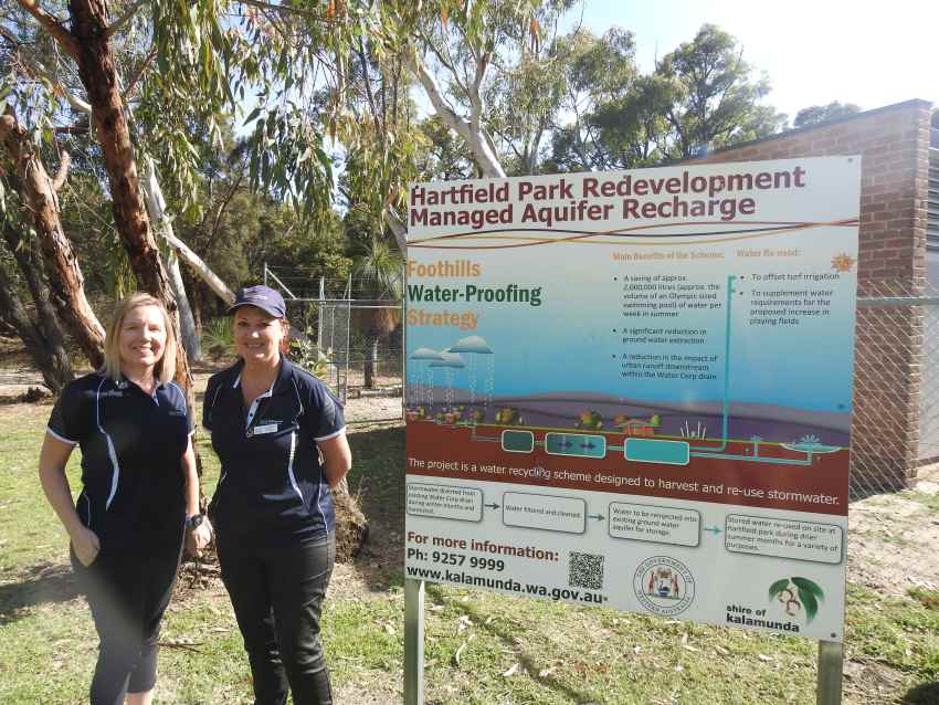 Two women stand next to a large sign outside, which demonstrates waterwise irrigation
